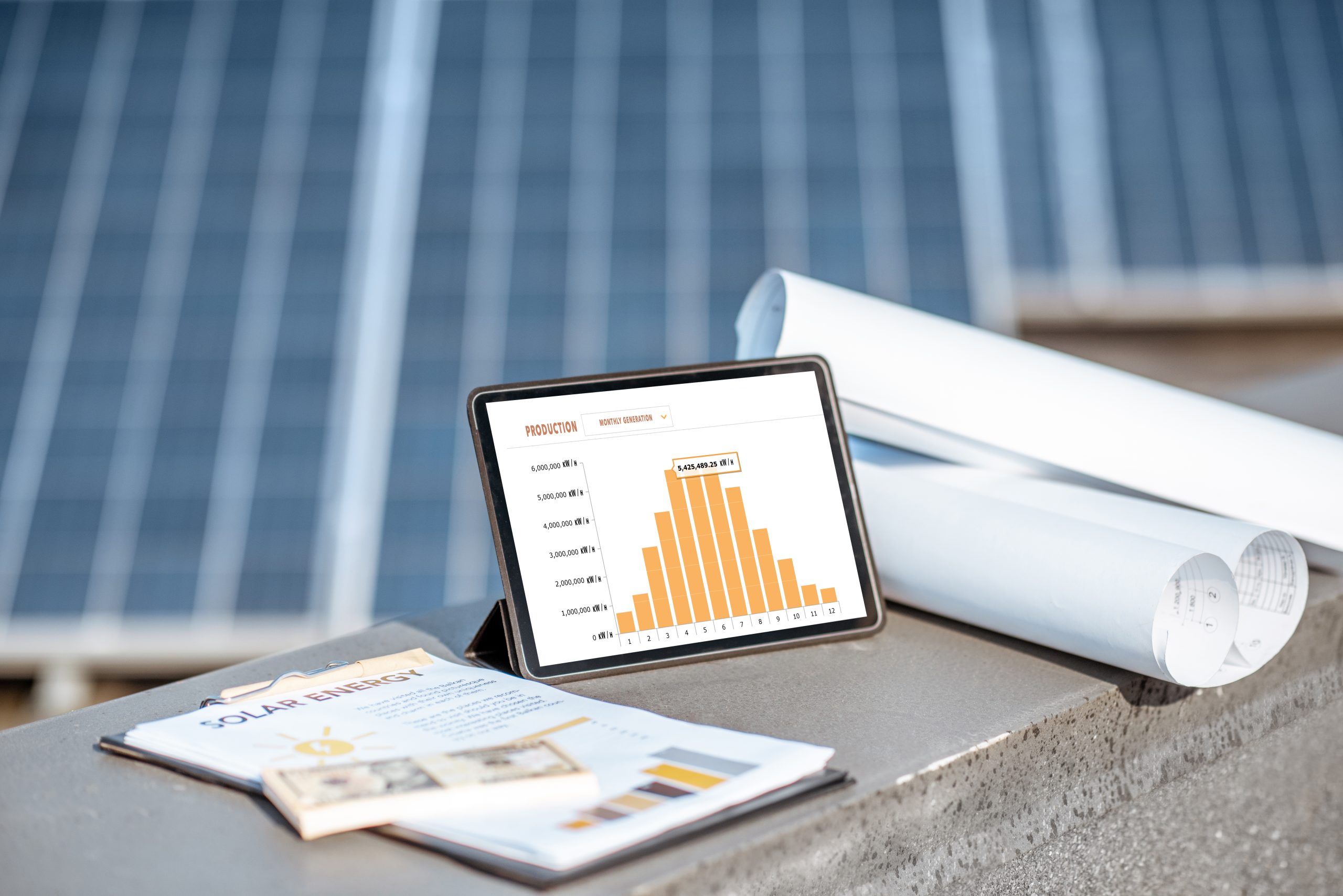 Composition of blueprints, money and digital tablet with a chart of electricity production on a solar power plant outdoors. Electricity production monitoring concept